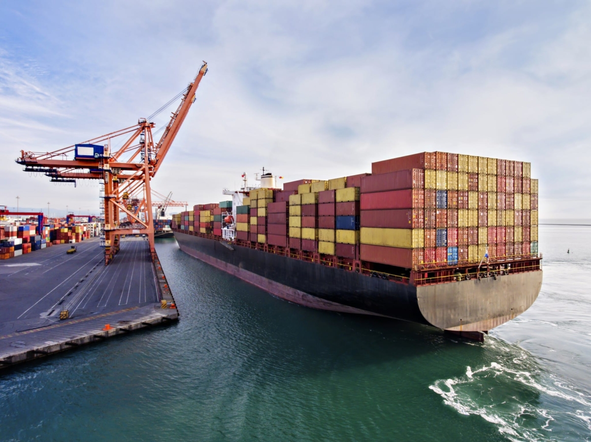 A boat with shipping containers arrives at a dock.