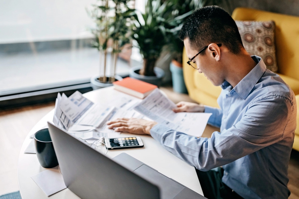 A man calculates inventory formulas with a calculator, laptop and reports.