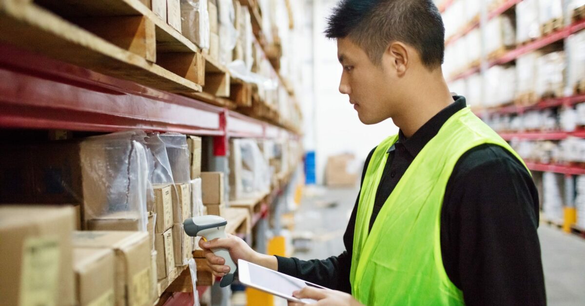 A man in a neon vest takes inventory using a barcode scanner.