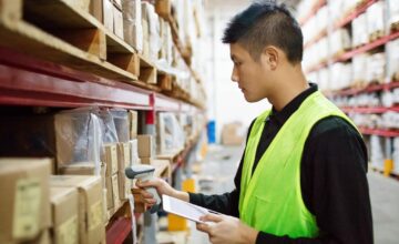 A man in a neon vest takes inventory using a barcode scanner.