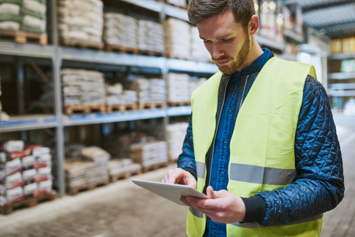 An employee wearing a visibility vest takes inventory on a tablet.
