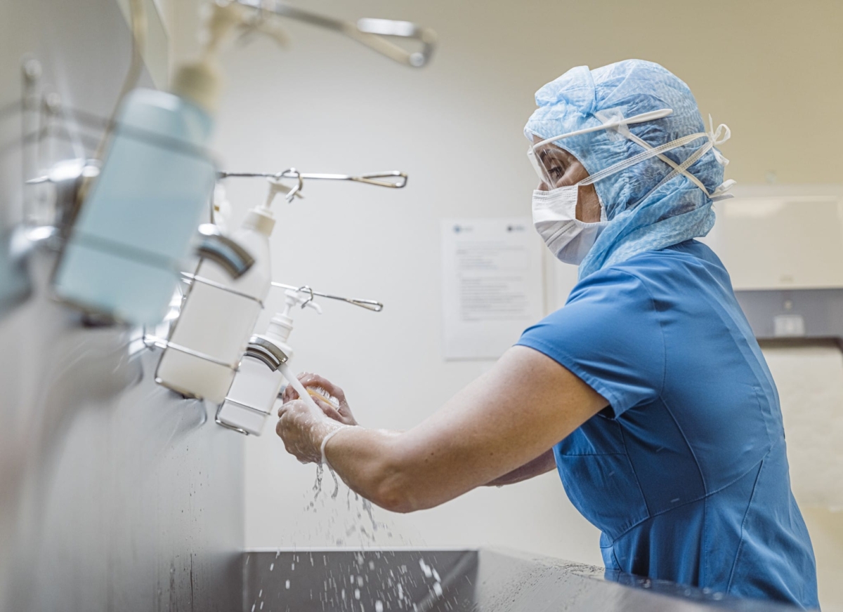 A doctor in scrubs and a face mask washes her hands.