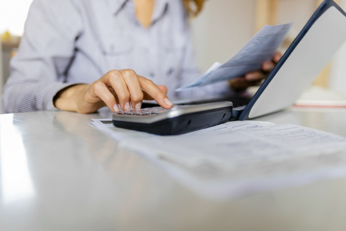 A woman uses a calculator near her laptop.