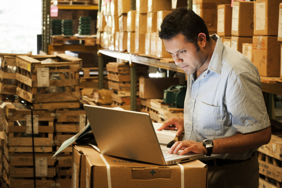 A man takes inventory in a stockroom using a laptop.