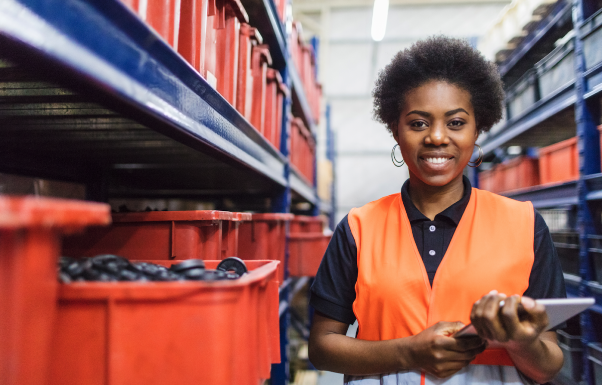 A woman is a stockroom smiles in a vest.