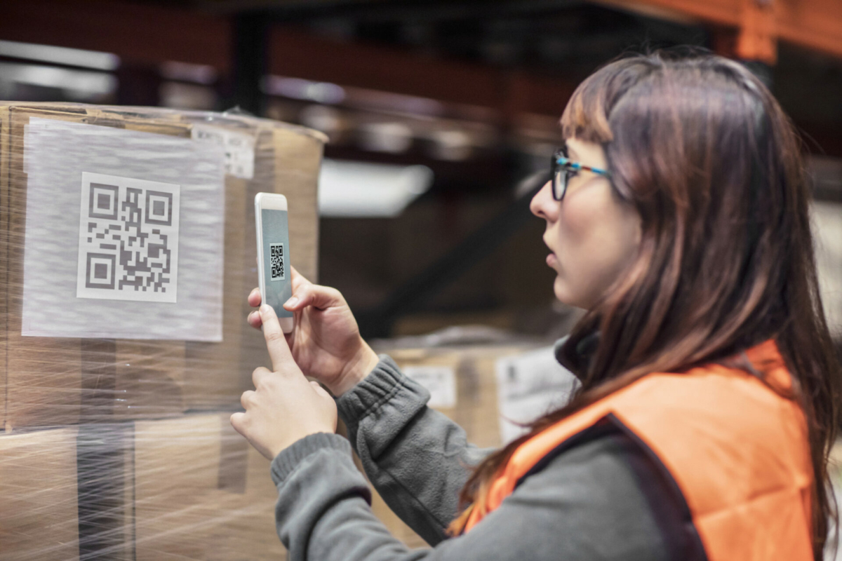 A woman in a visibility vest uses her phone to scan the QR code on a package.