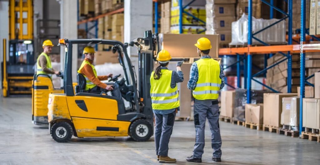 Two workers in neon vests work in a warehouse.