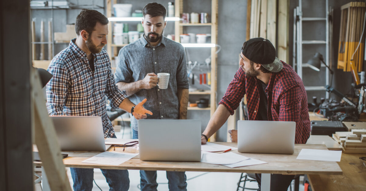 Three men in workshop comparing inventory systems costs