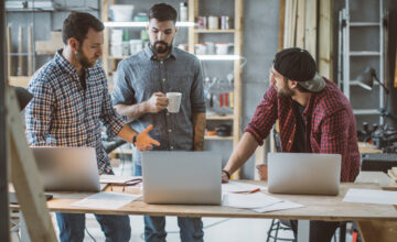 Three men in workshop comparing inventory systems costs
